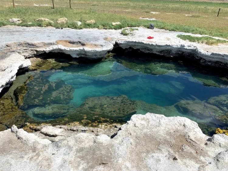Crystal clear deep geothermal pool at Meadow Hot Springs in central Utah desert with mountain views